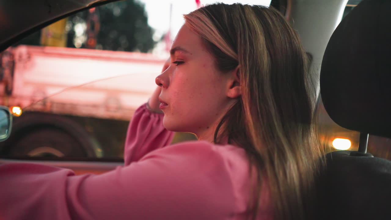 mujer sentada en su coche atrapado en el tráfico durante la noche con reflejos de luz roja suave brillando en su cara, una vista borrosa de otro vehículo se puede ver cerca con la luz borrosa del coche