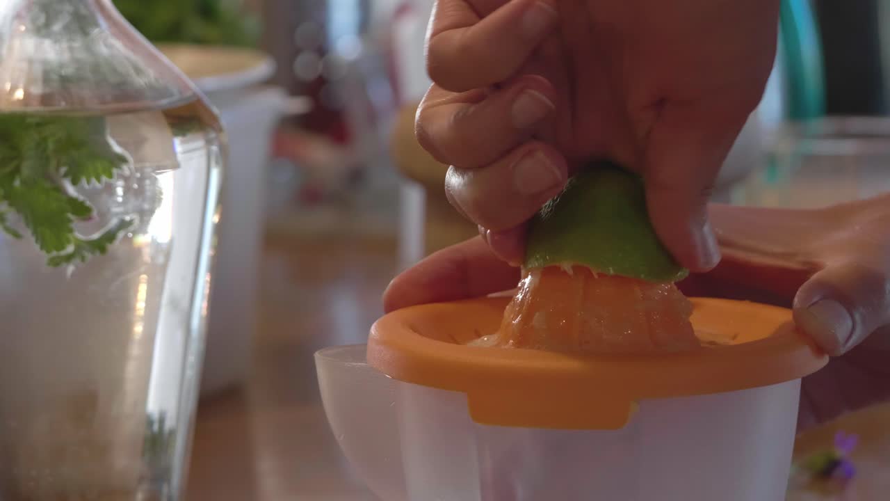 Primer plano de manos exprimiendo una lima verde en un exprimidor manual de cítricos naranja para extraer jugo fresco, demostrando preparación de alimentos saludables y técnicas de cocina natural.