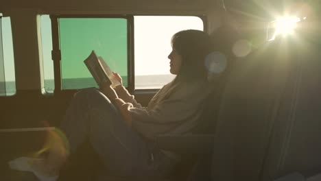 traveling woman reading book in van at sunset