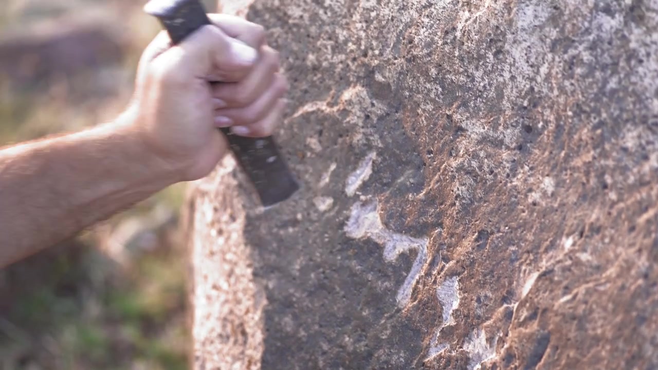 Person Using Stone Tool to Carve Petroglyphs on Rock