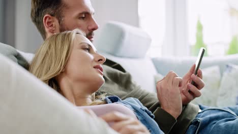 pareja aburrida usando el teléfono móvil y acostada en el sofá