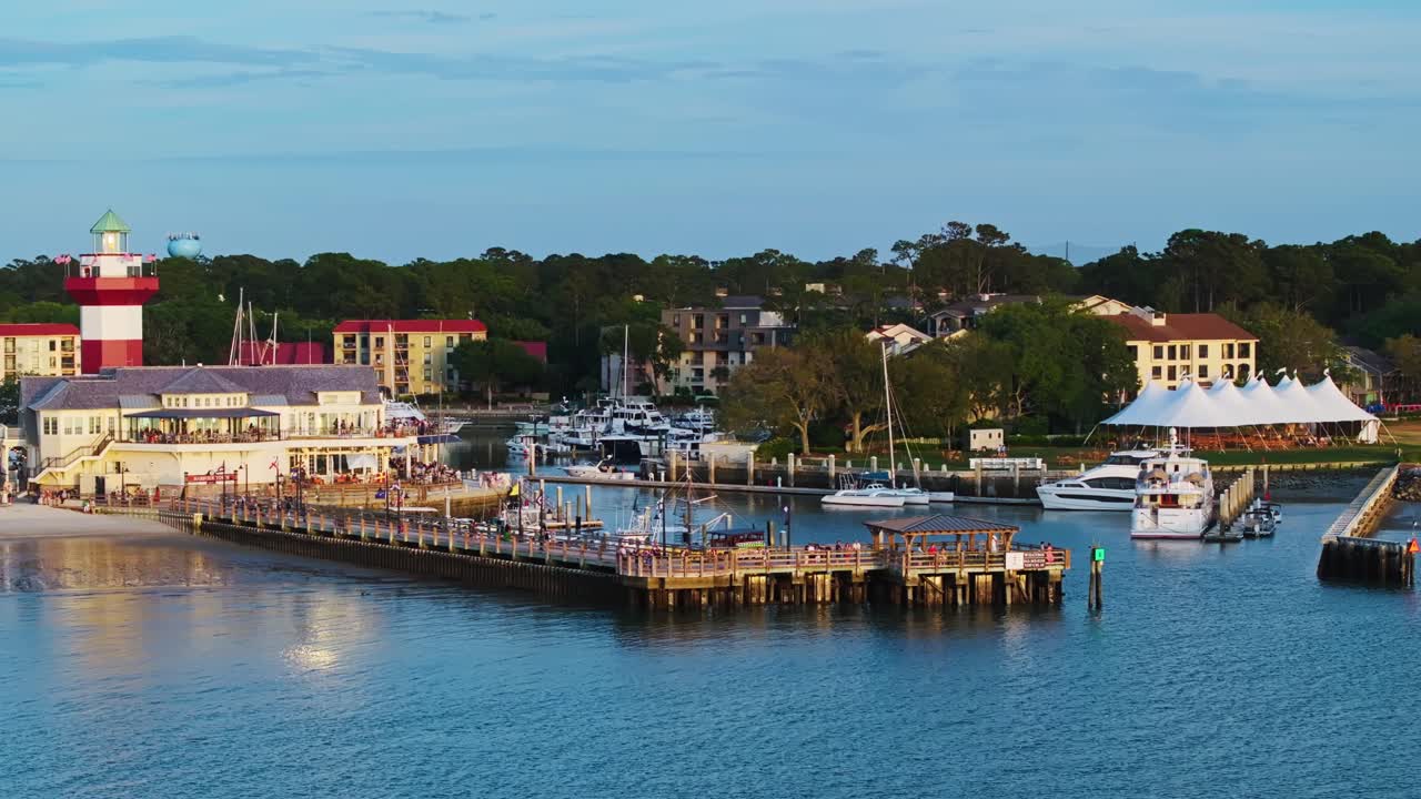 Drone pullback over boats near boardwalk and beachside buildings at harbor pier, Harbour Town Pier South Carolina USA
