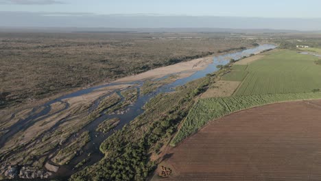 Imágenes-Aéreas-Y-De-Drones-Revelan-Granjas-De-Caña-De-Azúcar-Y-Pimientos-Contrastantes,-Divididas-Por-Un-Río-Estacional,-Que-Bordean-El-Parque-Nacional-Kruger.