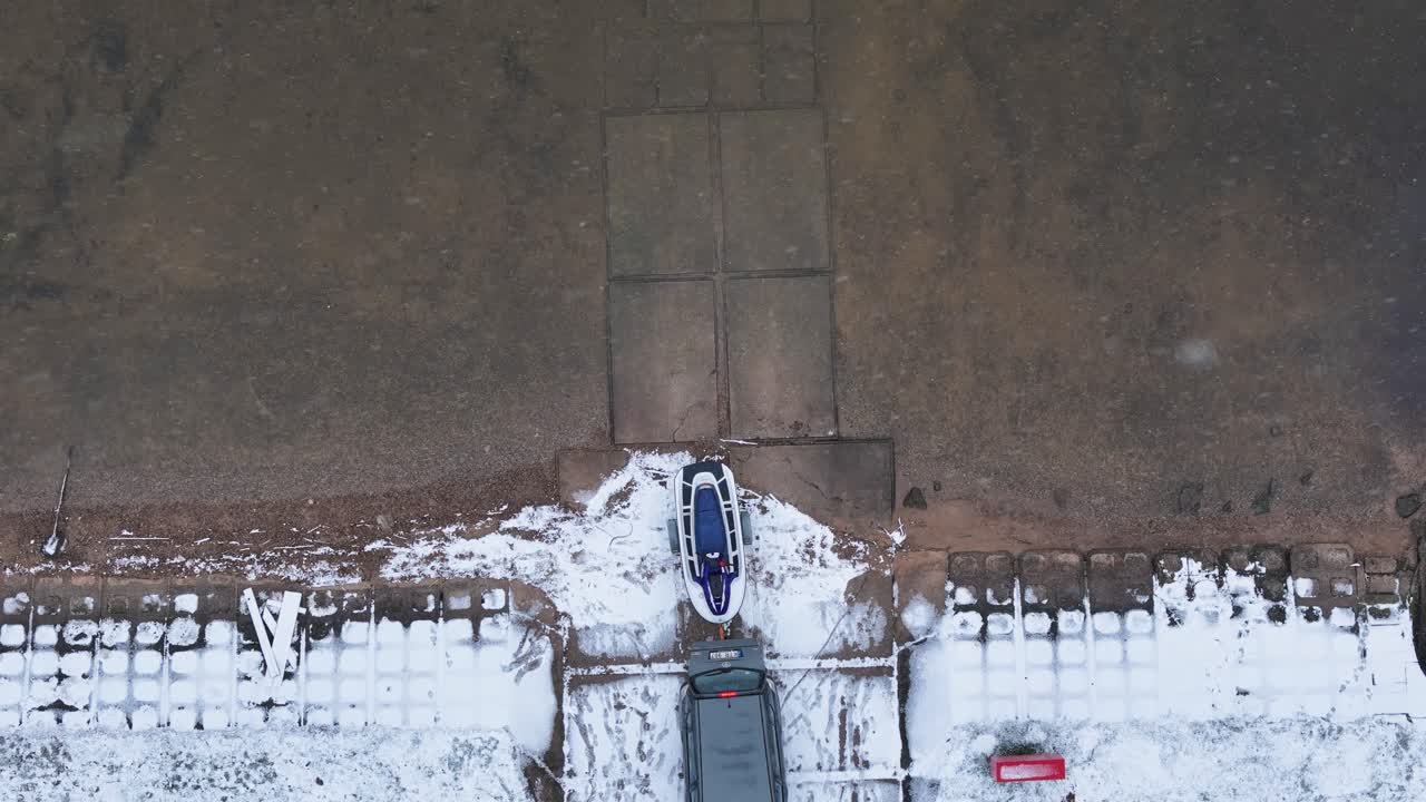 Aerial view capturing a car towing a boat on a trailer near the snowy Kauno Marios in Lithuania, highlighting winter boat storage and transportation in a serene, frozen landscape