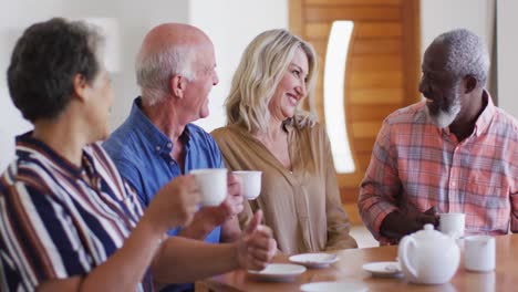 dos parejas mayores diversas sentadas junto a una mesa bebiendo té juntos en casa
