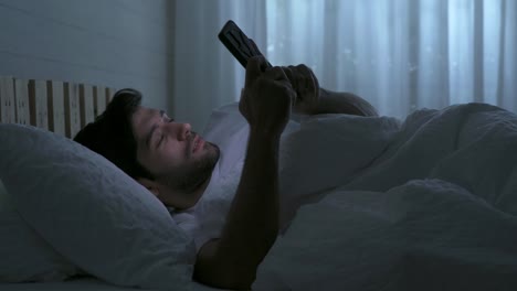 happy sleepy middle east young man. people using a smartphone on social media internet and sleeping on bed in bedroom at home. lifestyle on late night in technology device concept.