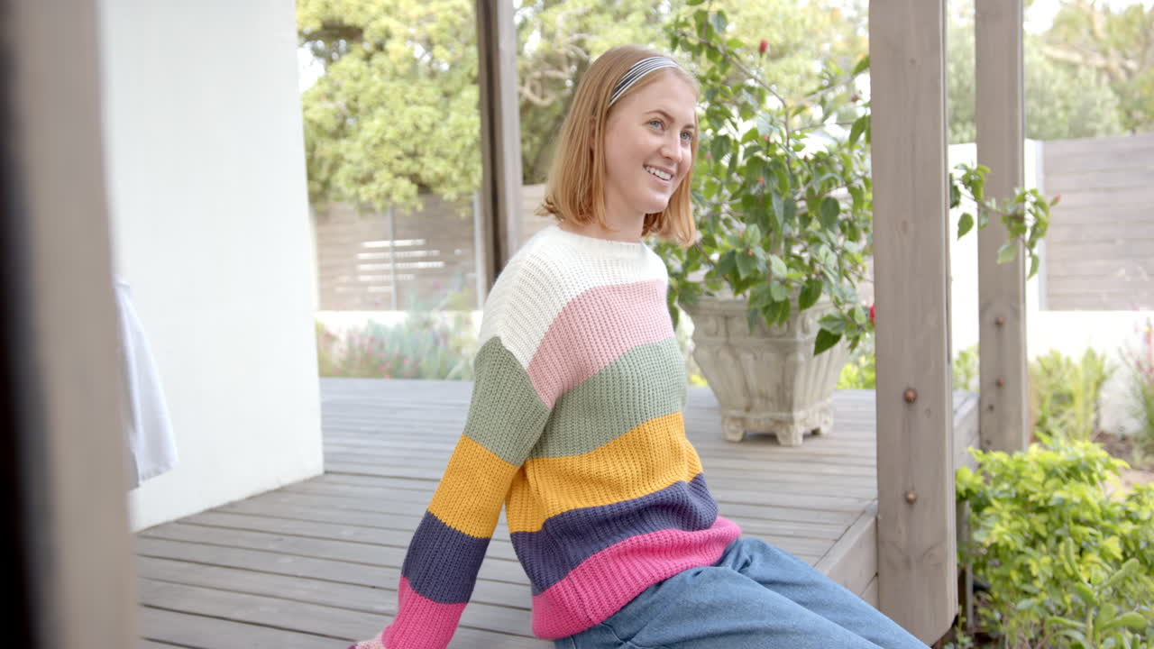 Smiling woman in colorful sweater sitting on porch, enjoying outdoor time