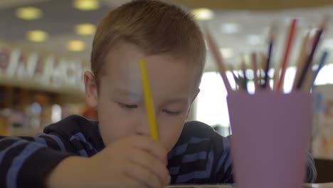 en la mesa sentado un niño pequeño y dibuja con lápices de colores