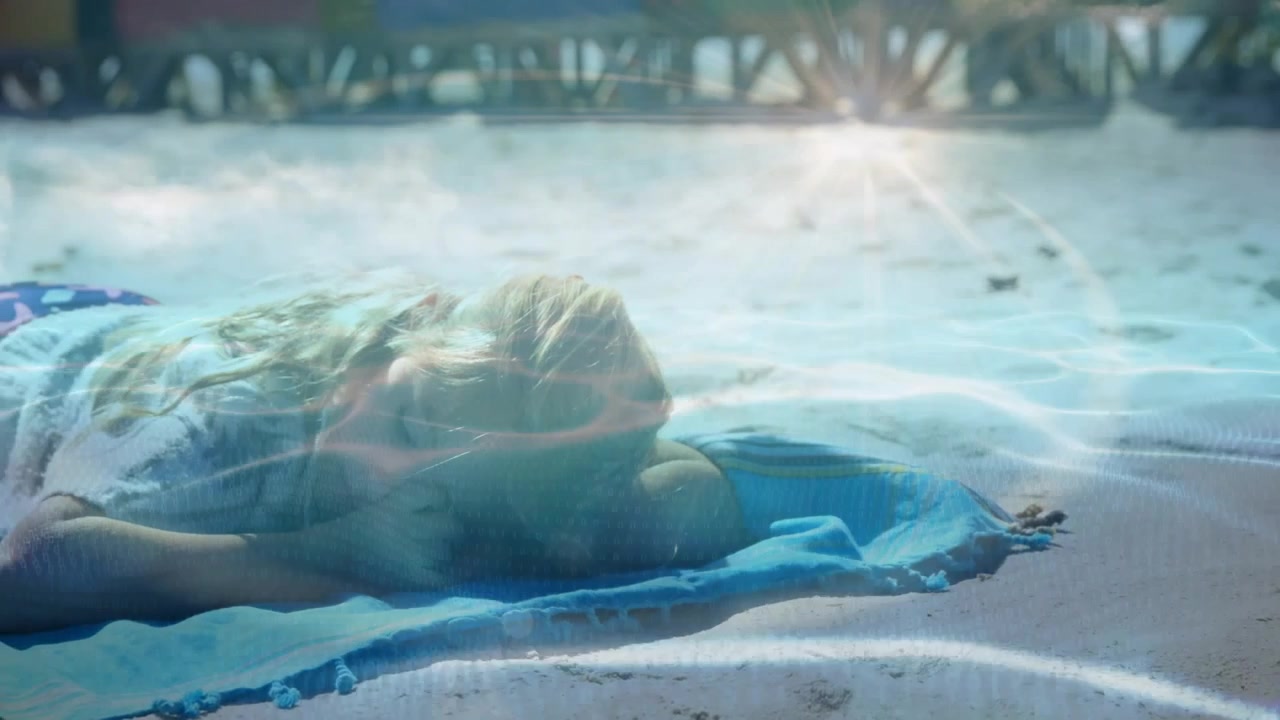 Girl lying prone on blue towel as camera panning, water-ripple sweeping over body for travel promo