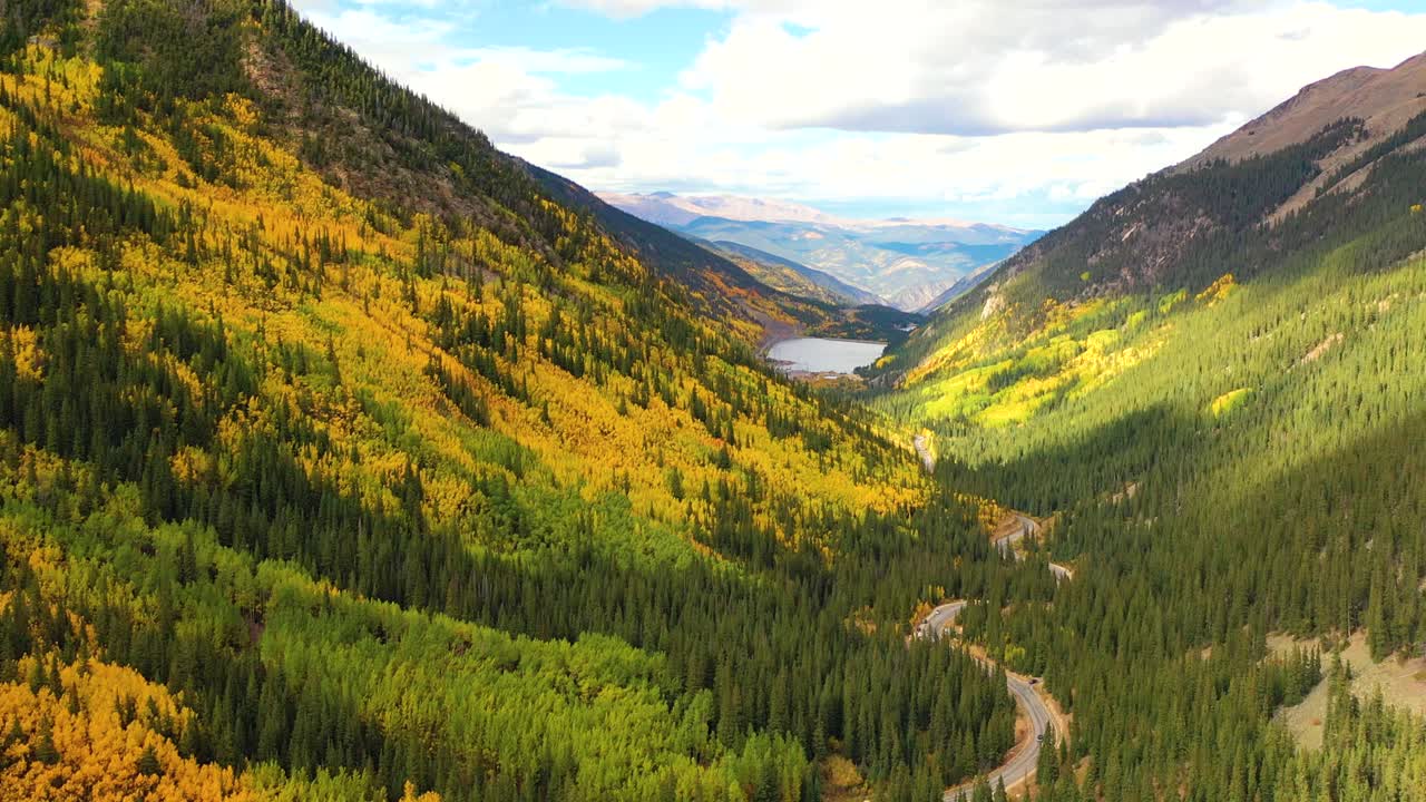 Glacier National Park in Montana bursts with color as forests of gold and green fill deep valleys below snow-covered peaks and winding roads cut through