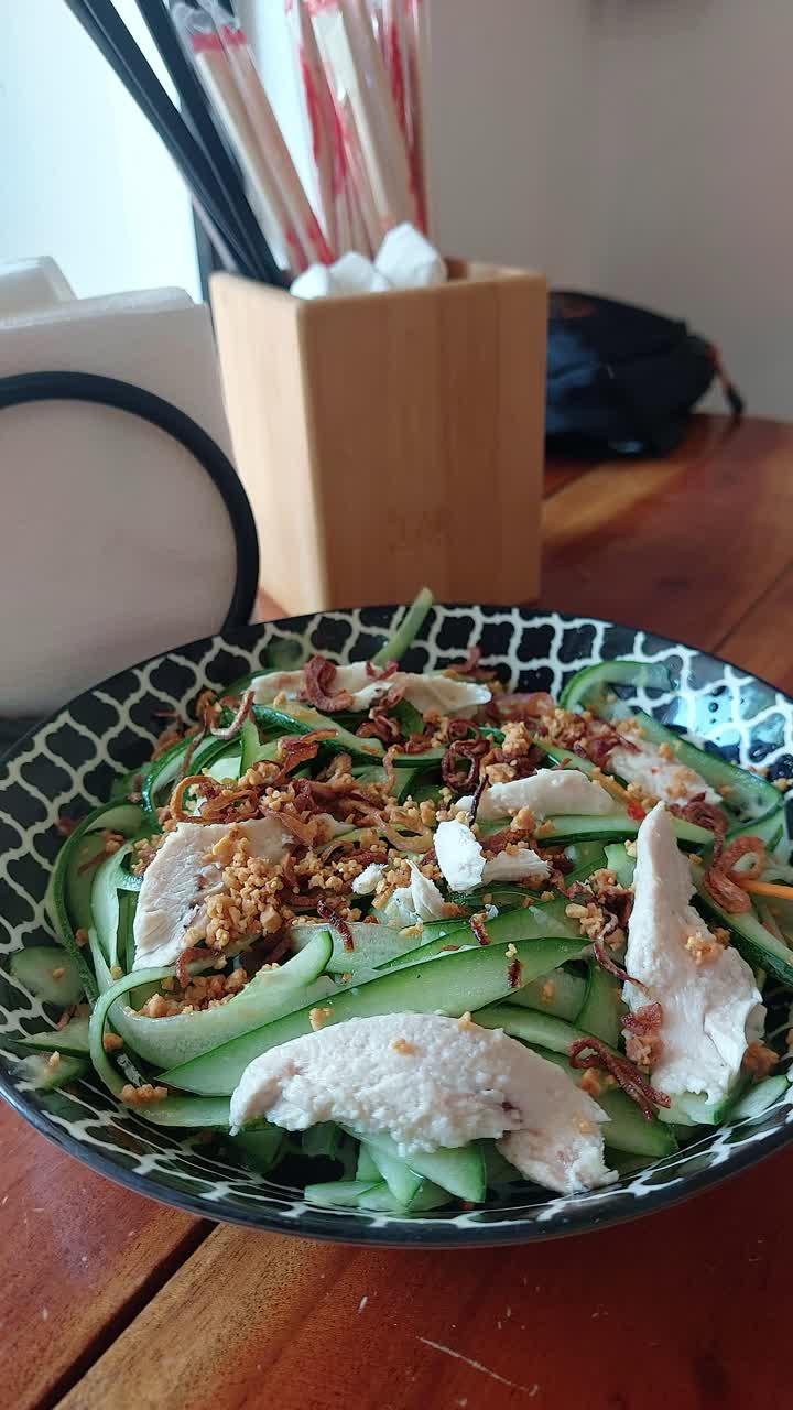 Eating a plate of thit ga goi tom or Vietnamese chicken cucumber salad topped with fried onions, authentic local food from Vietnam