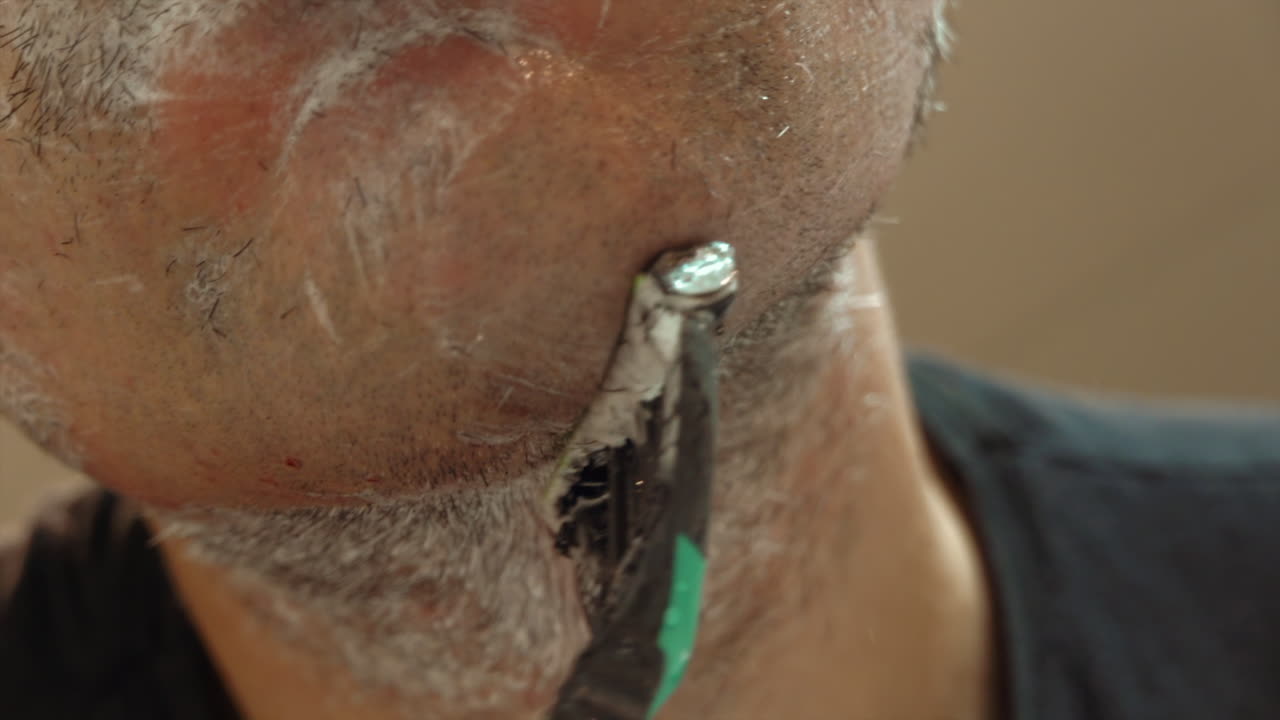 Close up of a man shaving his beard with a green and black razor