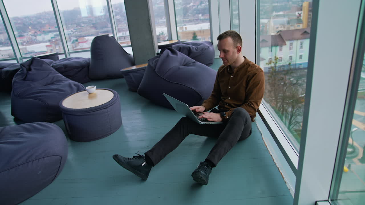 Young man with laptop sitting on floor by the window