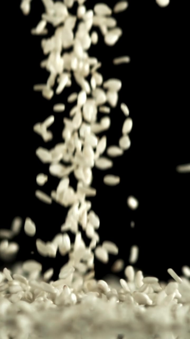 Chicchi di riso bianco che cadono e si accumulano su sfondo nero
