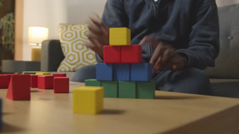 boy at home playing with colourful wooden building blocks