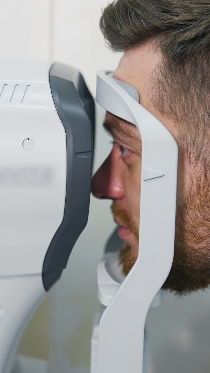 Patient man looks at device in ophthalmology clinic. Profile of patient's face looking into apparatus for eyes diagnostic in clinic. Close-up. Vertical video