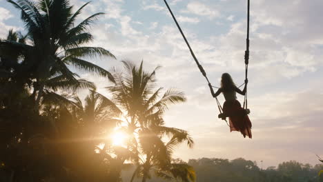 Zeitlupenreisende-Frau-Schwingt-Bei-Sonnenaufgang-Auf-Einer-Schaukel-Im-Tropischen-Regenwald-über-Den-Dschungel,-Während-Die-Sonne-Durch-Die-Palmen-Scheint,-Urlaubslebensstil-Und-Freiheit