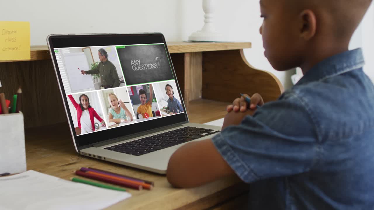 Schoolboy using laptop for online lesson at home, with diverse teacher and class on screen