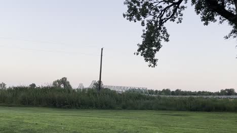 Weitwinkelaufnahme-Einer-Wiese-Mit-Einem-Ast-Im-Vordergrund-Und-Einer-Brücke-Im-Hintergrund