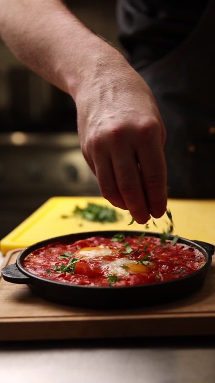 Chef che guarnisce Shakshuka appena cucinata con erbe aromatiche