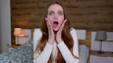 upset young woman in white blouse raising hands in anger and shouting wow, touches cheek, open mouth