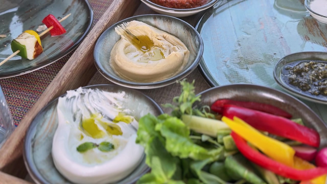 Un primo piano di un piatto mezze tradizionale mediorientale con hummus, labneh e verdure fresche. Il cibo appetitoso è servito in ciotole di ceramica rustiche su un vassoio di legno in piena luce diurna