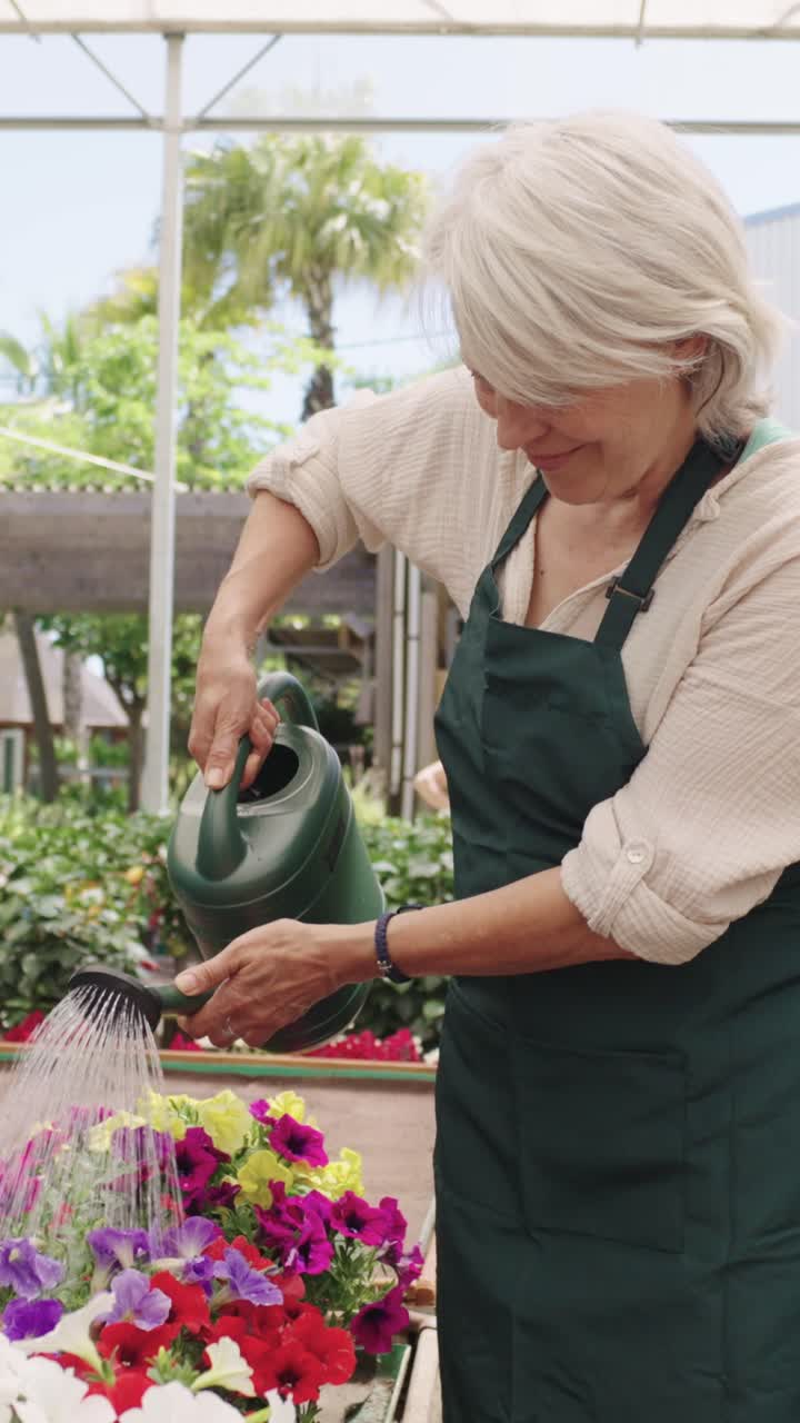여성 이 온실 에서 꽃 에 물 을 주고 있다