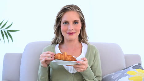 una mujer alegre comiendo un croissant.