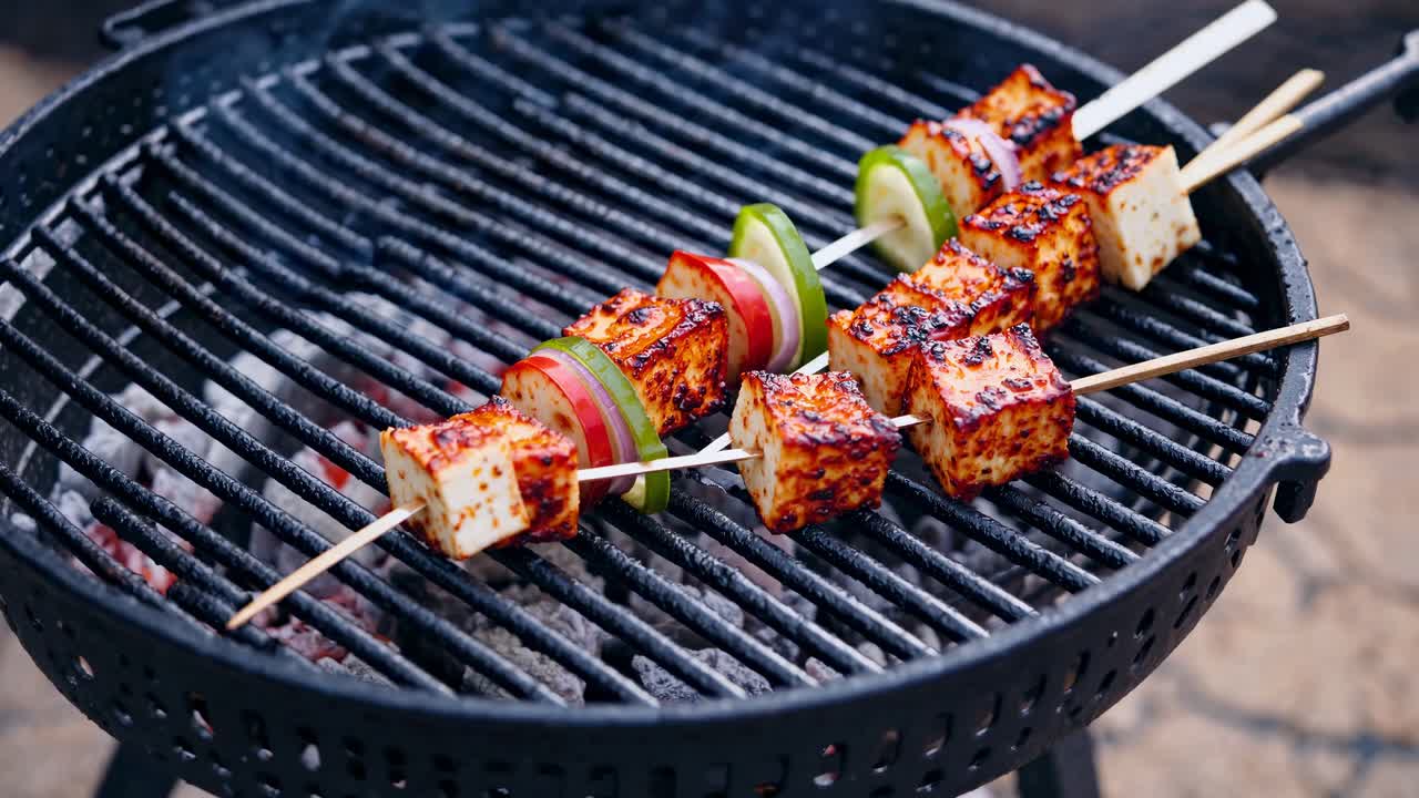 Videon lähikuva grillatuista vartaista paneer-juustolla ja vihanneksilla pyöreällä grillillä.