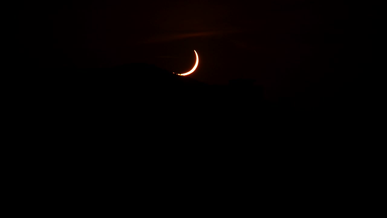 Pequeno crescente brilhante brilha perto do centro superior contra um céu preto profundo, com uma névoa vermelha fraca e forte contraste, criando um clima celestial isolado, visual minimalista, atmosfera tranquila e amplo vazio