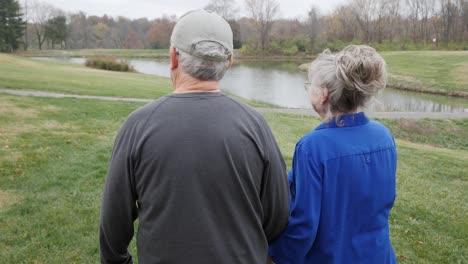 siguiendo a una pareja de ancianos caminando hacia el estanque en el parque en un día de otoño