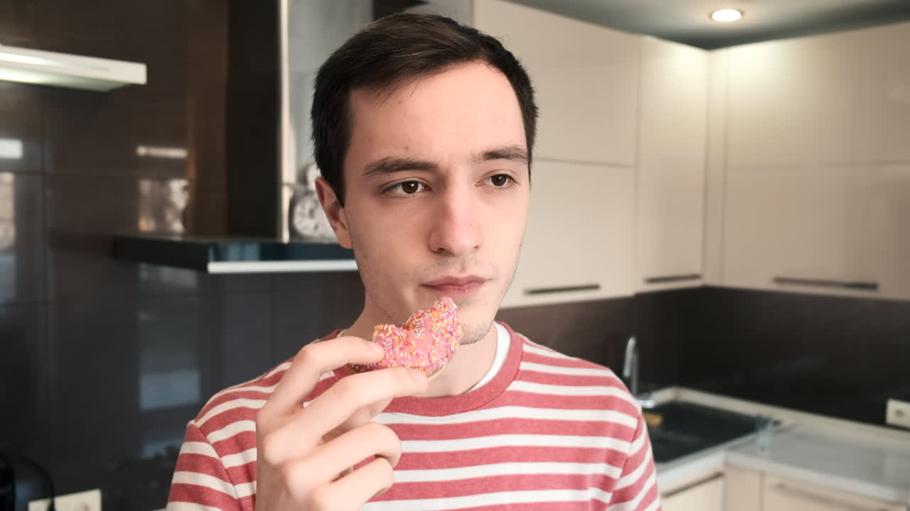 A man eating a rose donut on the kitchen