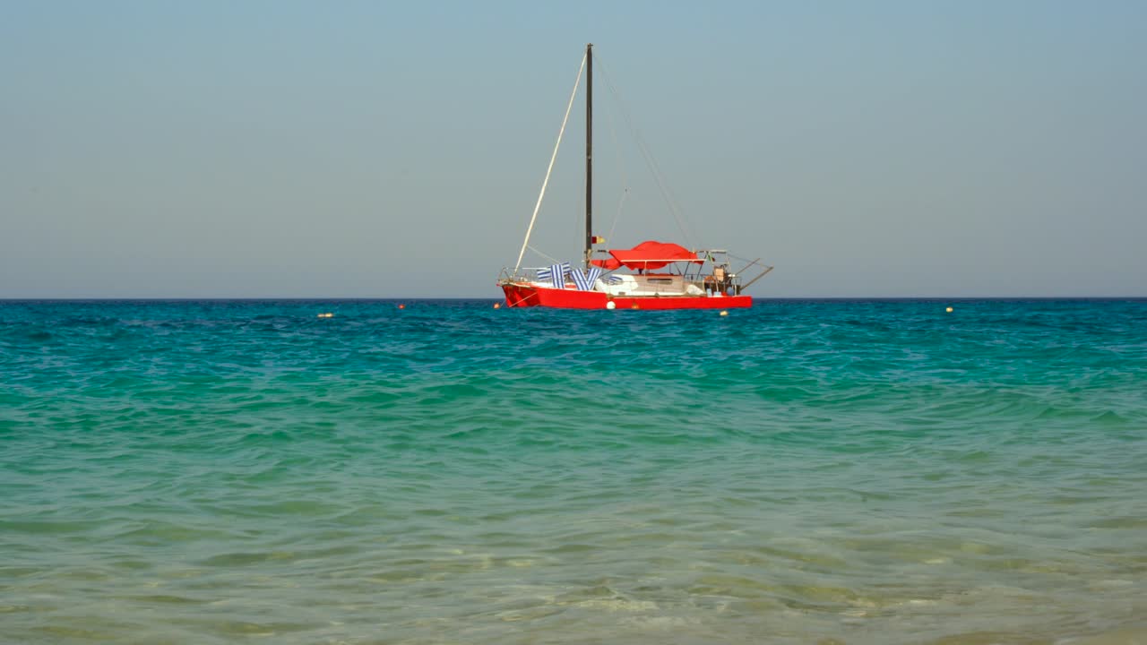 여름 휴가 날에 푸른 청록색 물로 이오니아 해 연안 근처에 붉은 쌍동선이 뜬다