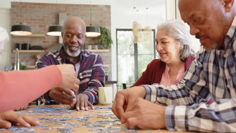 Happy-diverse-senior-female-and-male-friends-talking-and-doing-jigsaw-puzzle-in-kitchen,-slow-motion