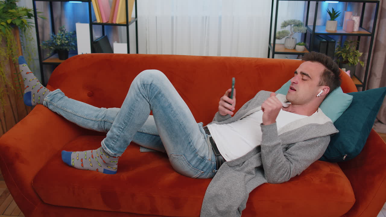 행복하고 편안한 남자, 무선 이어폰으로 춤추고, 좋아하는 음악을 듣고, 집에서 소파에 누워