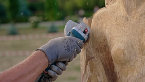 Hands of unrecognized person in gloves hold a grinding tool. Electric instrument working with piece of wood.