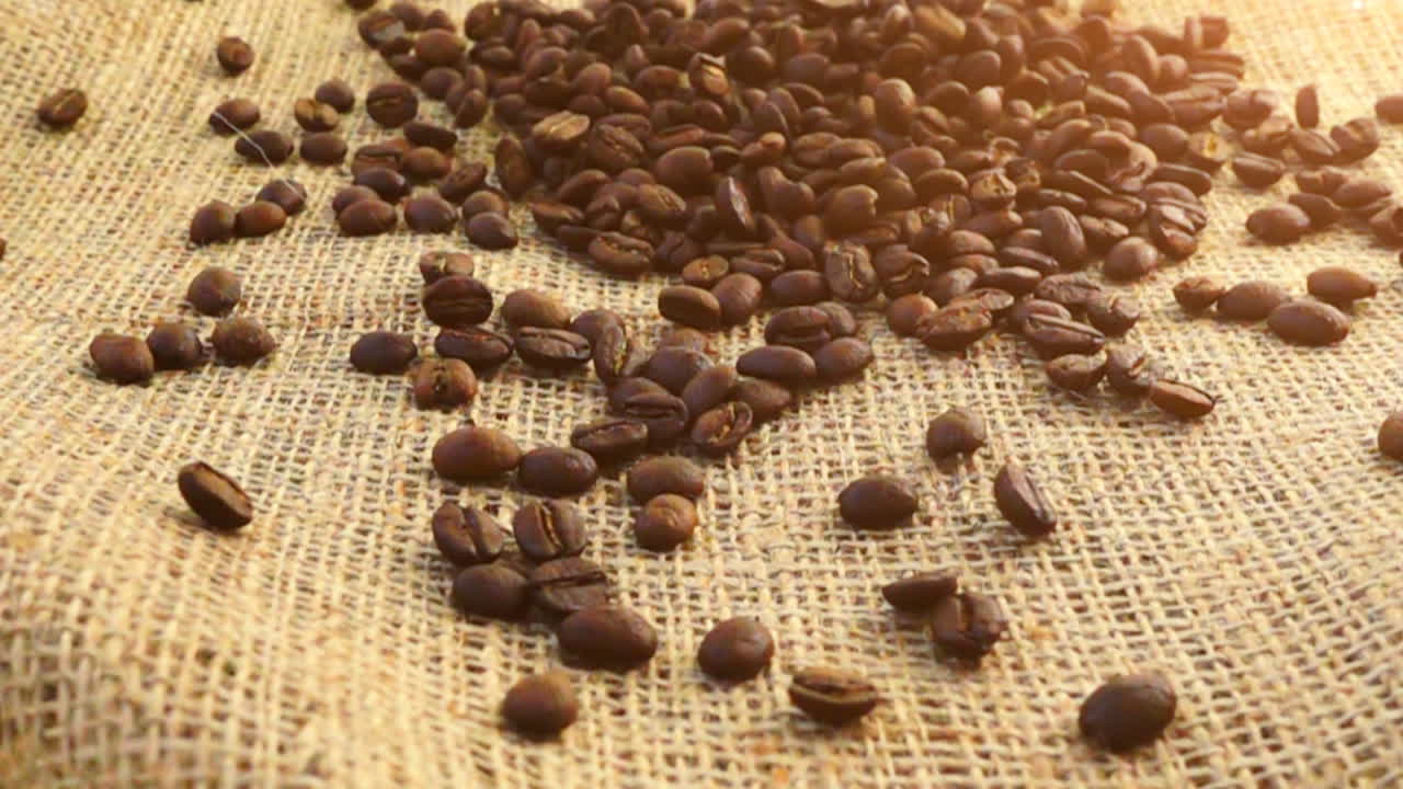 Chicchi di caffè cadono su tela di iuta al rallentatore.