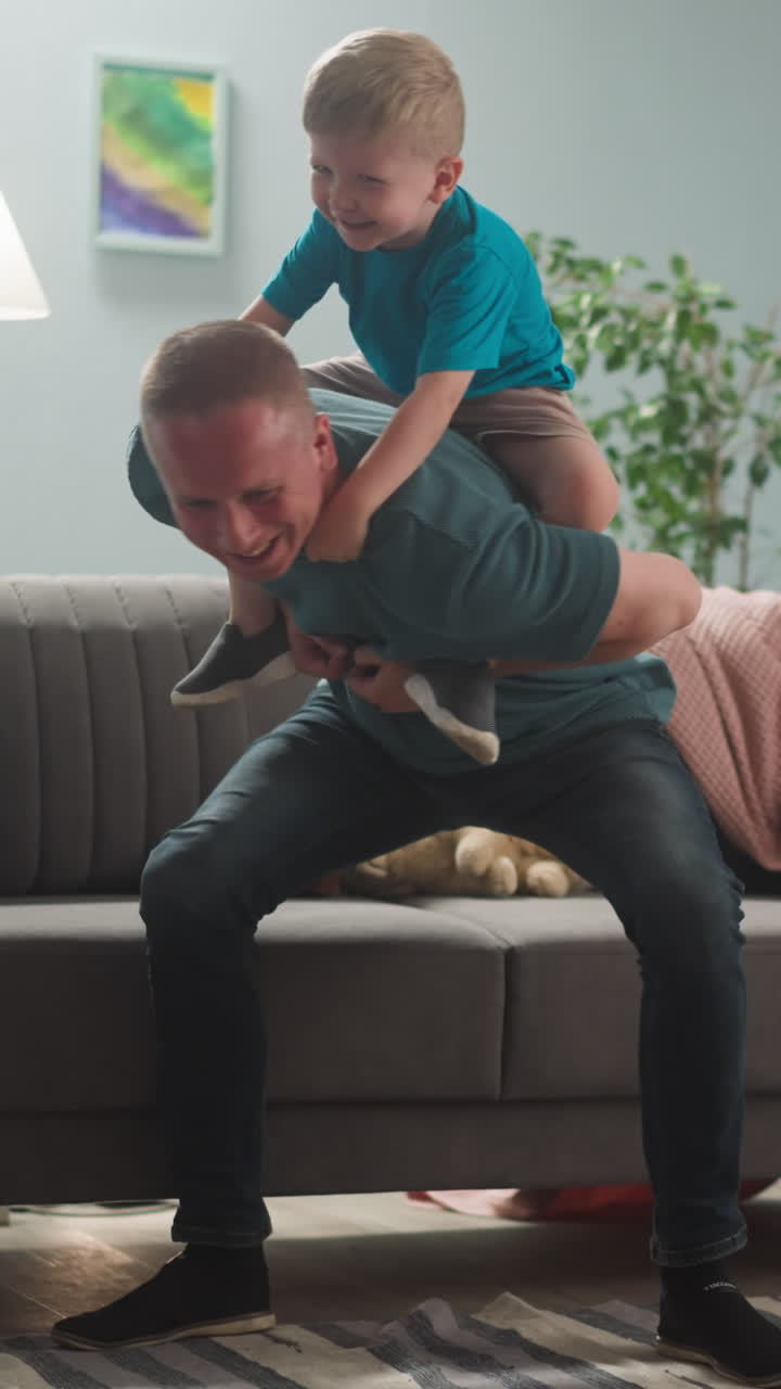 young man plays with young man plays with child in bright room in blue tones, they laugh, dad rolls his sons on his backchild, laughs, dad rolls his sons on his back
