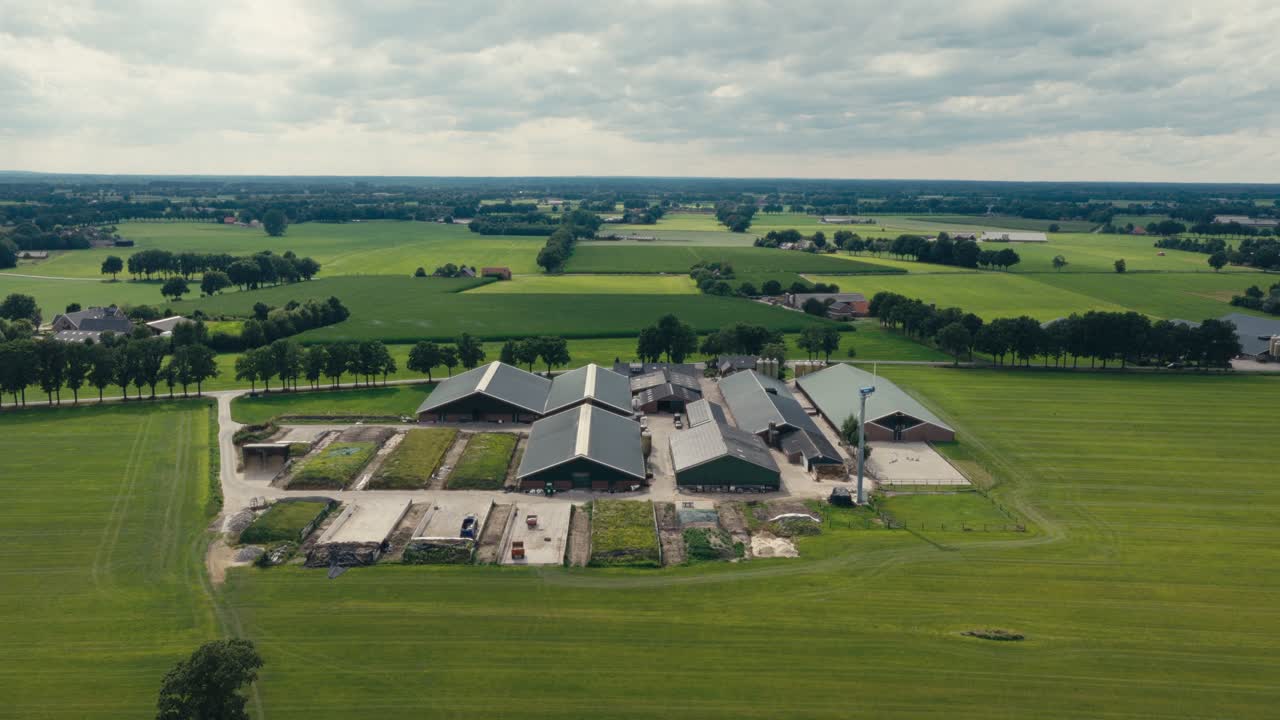 Drone shot of a large farm complex with green rooftops and surrounding fields under a clear sky in the countryside