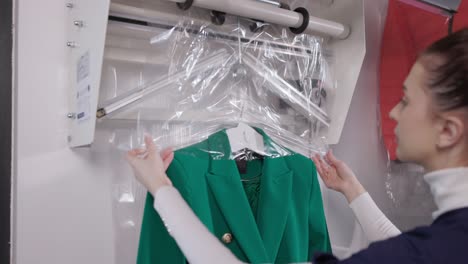 traje de embalaje de trabajadora femenina con lavadora de ropa en la máquina de empacado después de la limpieza en seco