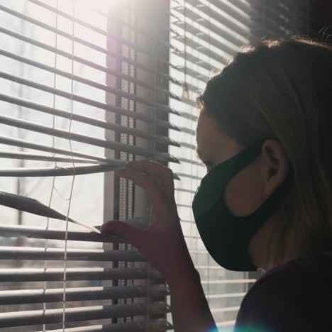 A-Woman-In-A-Protective-Mask-Peeks-Out-Of-The-Window-Of-Her-Apartment