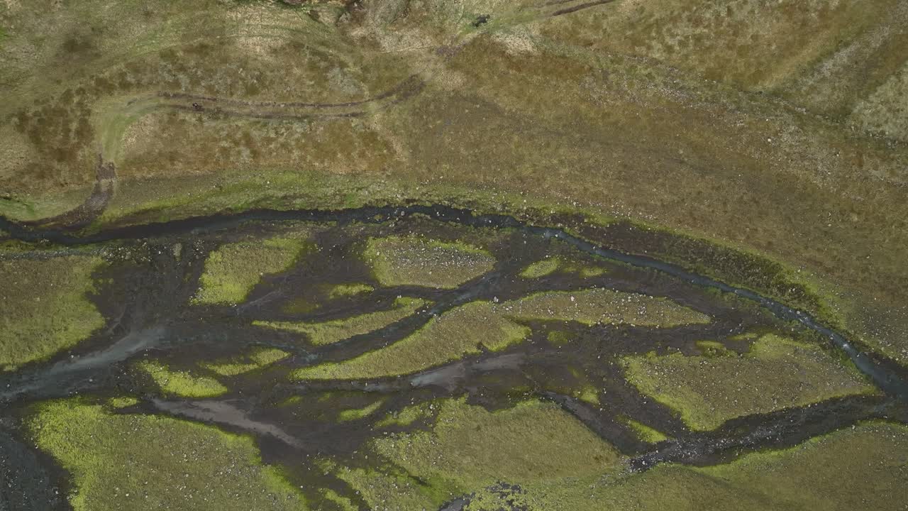 Aerial view of a braided river system in North Iceland, with dark waters winding through moss-covered terrain, creating intricate natural patterns.