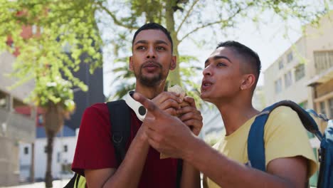 two happy mixed race friends eating and talking in the street