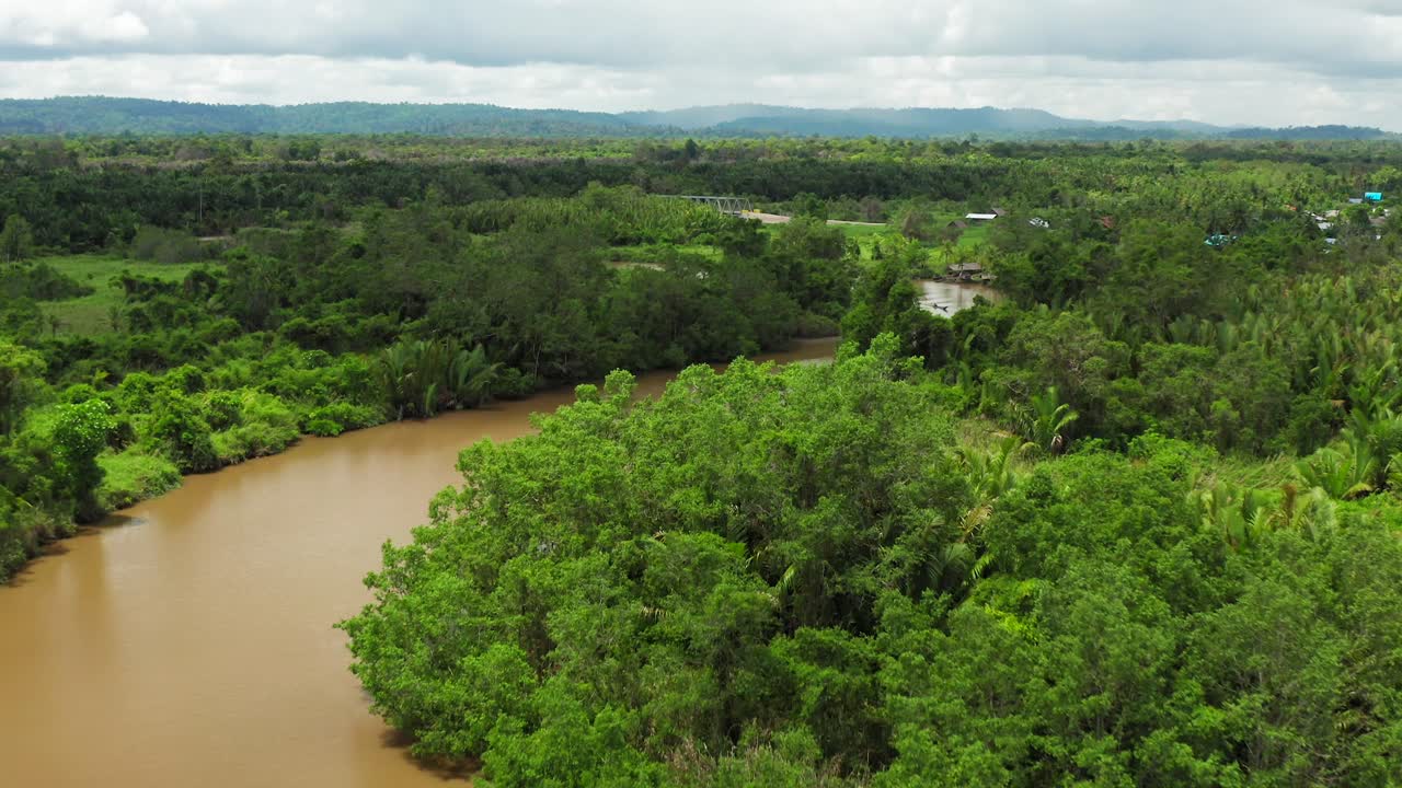 Aerial flight above murky Indonesian twisting through lush green jungle