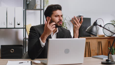 Indian-business-man-working,-having-mobile-phone-talk-at-office-workplace-using-messenger-chat-apps