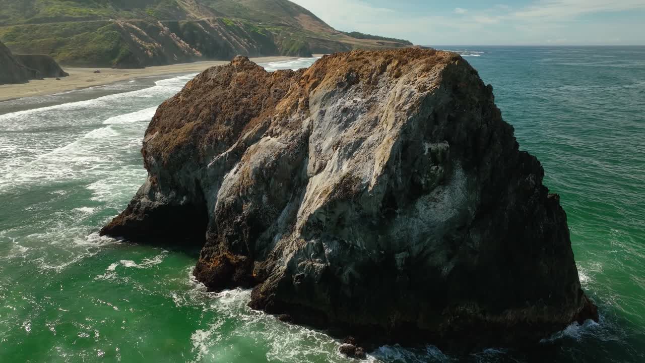 vista aérea de una gran roca sentada en el agua de la costa de california, erosionándose lentamente