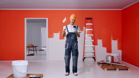 full body of asian man painter wearing safety helmet looking at smartphone then screaming goal celebrating while standing with painting wall in room