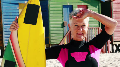 Senior-woman-with-surfboard-standing-on-beach