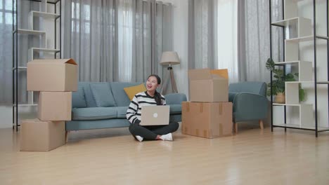 woman working on laptop amidst moving boxes in a new home.