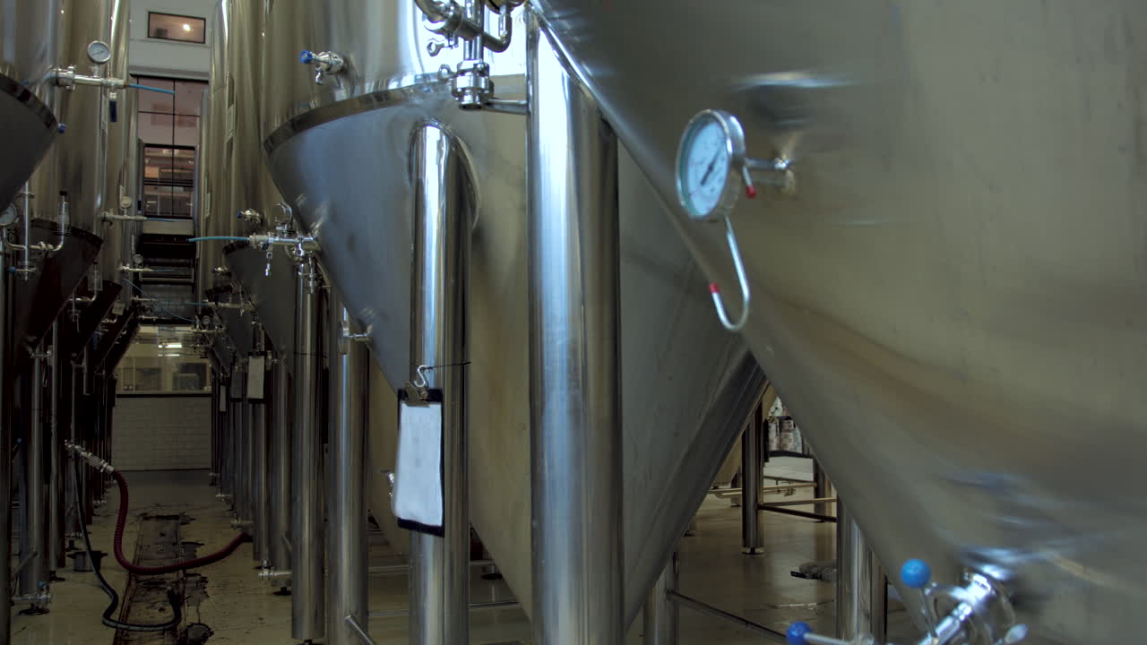 Slow pan right from large stainless steel beer fermentation tanks in a brewery to a close shot of a pressure gauge